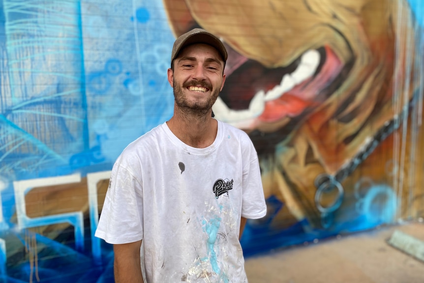 a young man smiling in front of street art