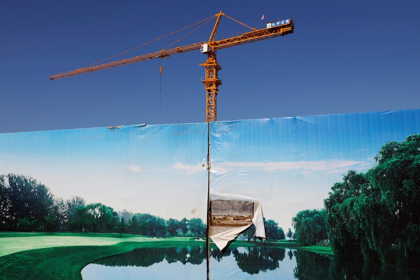 A crane stands behind a gate to the construction site of a luxury residential compound