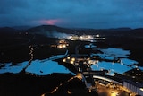 A deep blue lagoon at night, light up by lighting and a red glow from a nearby mountain.