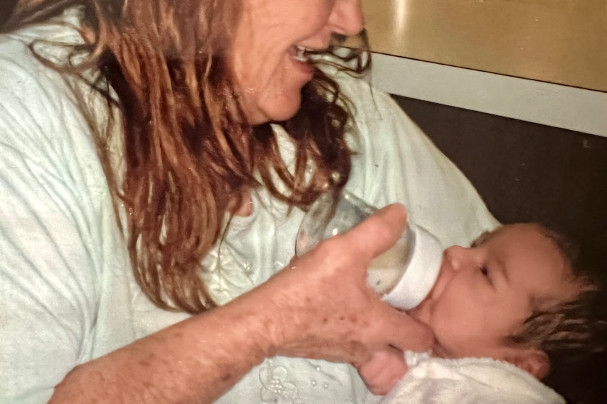 A grandmother holds a newborn baby and feeds her with a milk bottle. 
