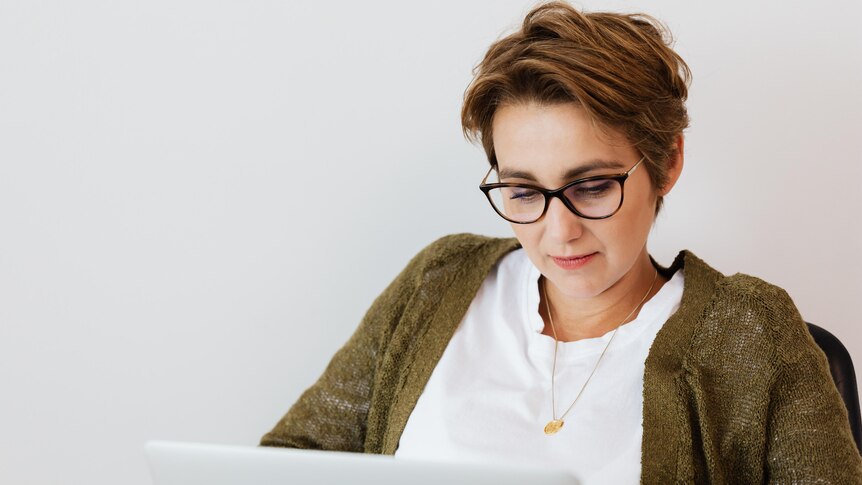 A woman wearing a green cardigan and glasses looks at a laptop screen.