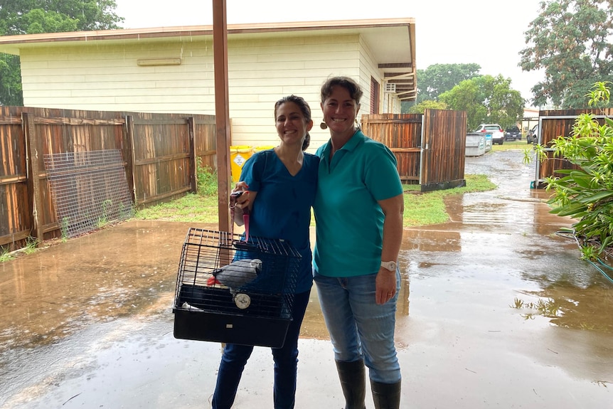 Sarah McLay and Amanda Shannon stand together under cover as rain falls outside