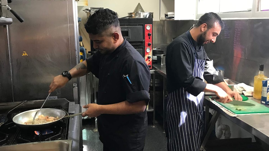 Two chefs cooking and chopping food in a pub kitchen.