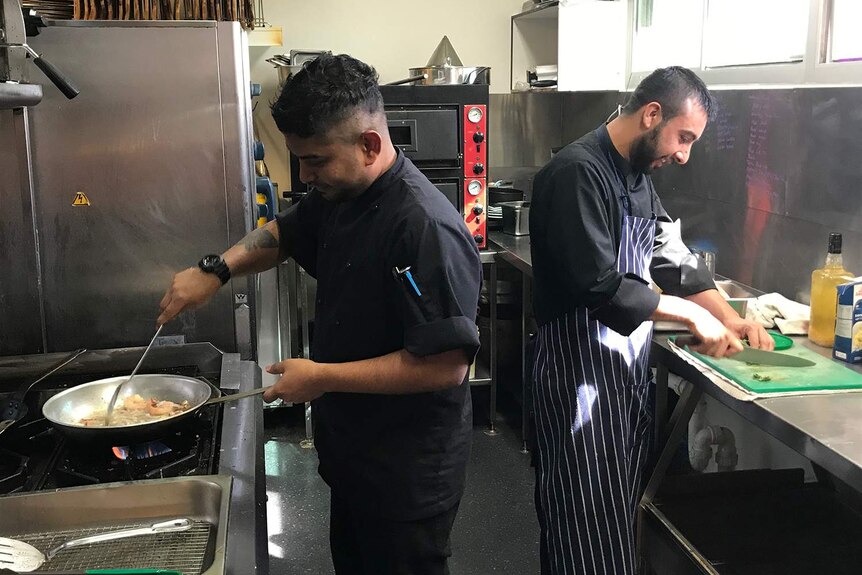 Two chefs cooking and chopping food in a pub kitchen.