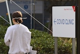 A woman stands outside a COVID-19 testing clinic with her back to the camera.