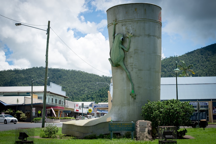 A sculpture of a giant gumboot with a frog clinging to its side in a small town.