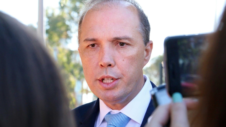 Photo between two people of Peter Dutton speaking during a door-stop outside Parliament House.