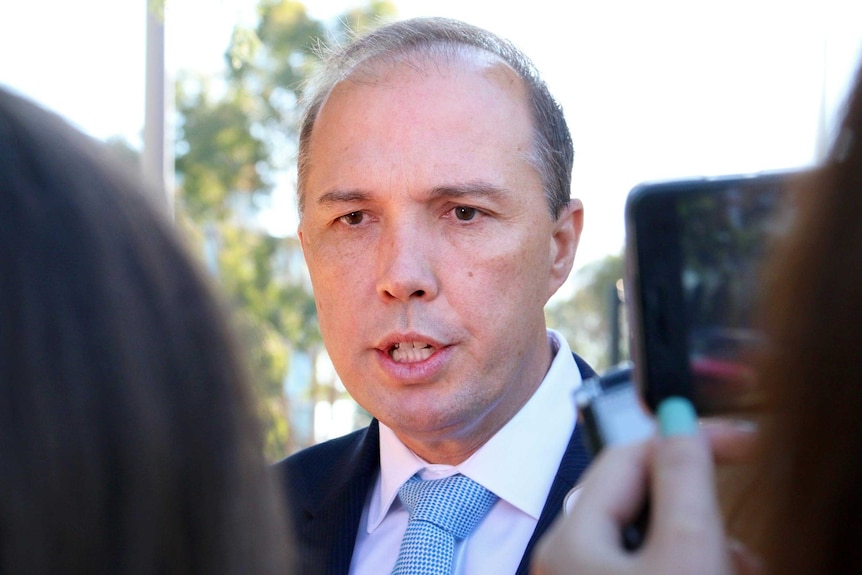 Photo between two people of Peter Dutton speaking during a door-stop outside Parliament House.