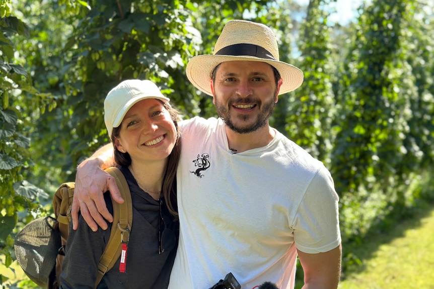 a young woman and a man smiling at the camera with hops vines in the background.