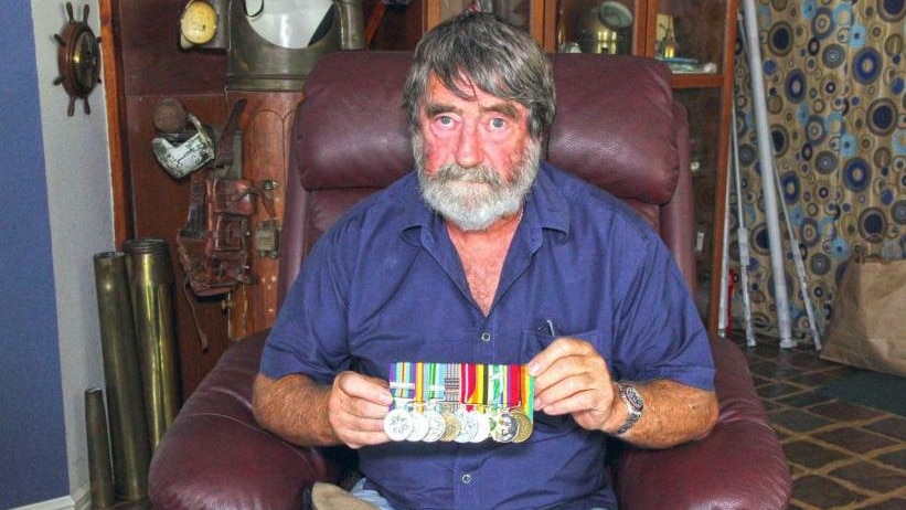 man with grey beard and wearing a blue shirt holding war service medals