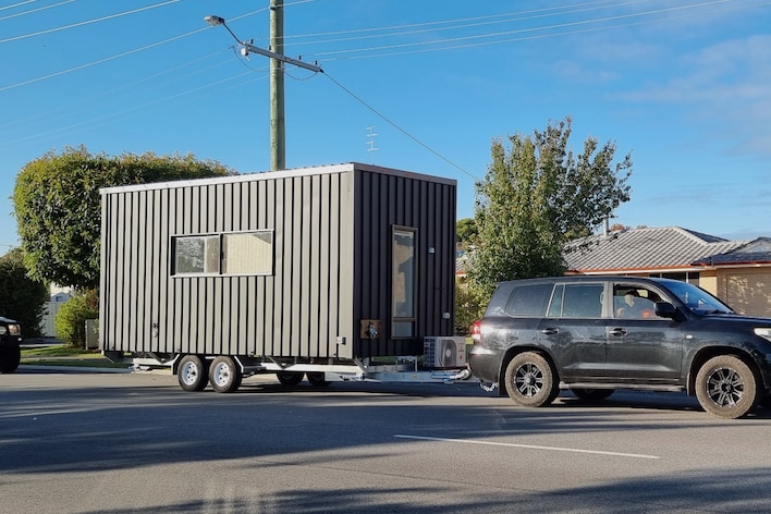 A small black tiny home on a trailer pulled by a four-wheel-drive vehicle.