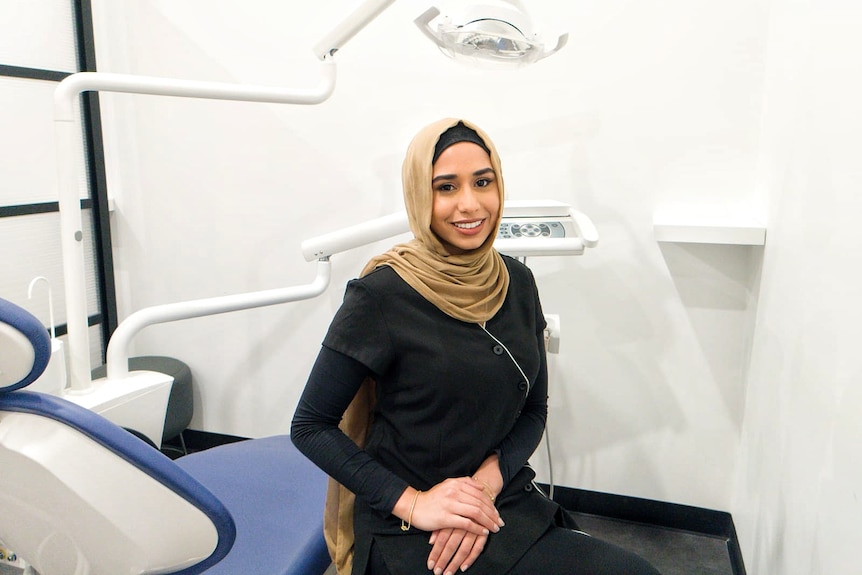 A woman in a hijab sits on a dentist chair. 