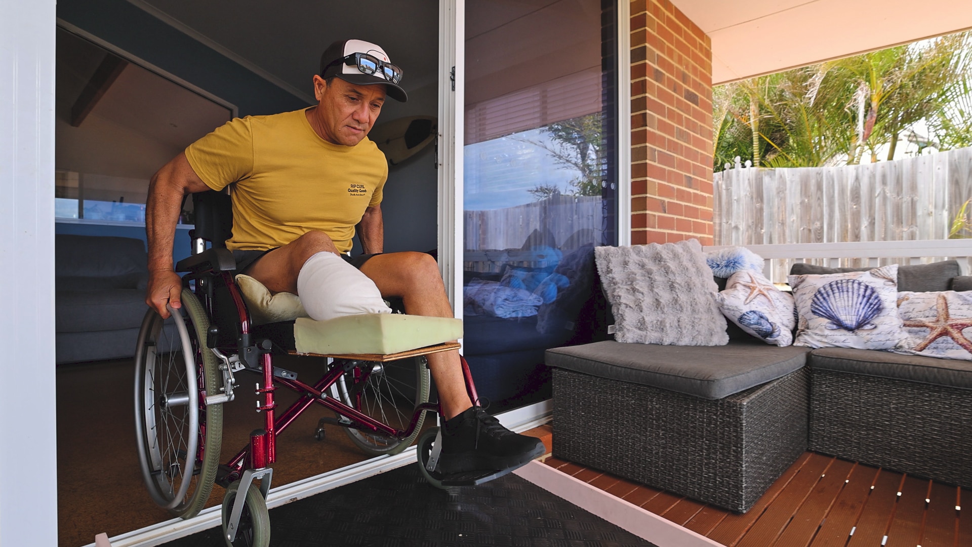 A man in a wheelchair with an amputated legs wheels himself down a ramp from a patio doorway.