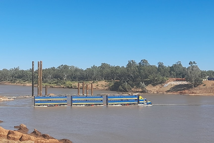 a triple road train is in deep water crossing a wide river