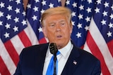 Donald Trump spreads his arms as he stands at the lecturn at the White House in front of American flags