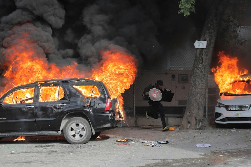 a man runs between cars that are ablaze in haiti