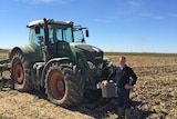 Poppy Growers Tasmania president Glynn Williams stands in front of a large Fendt tractor in a ploughed paddock in Spain