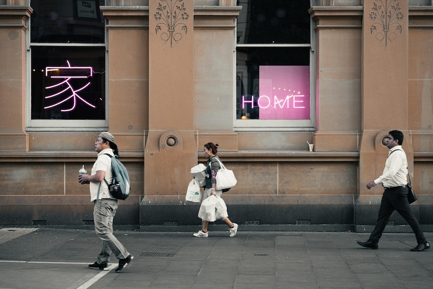 A photo of three people walking in front of pink neon signs in Sydney's Chinatown.