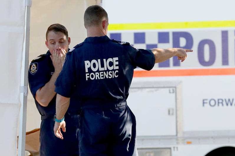 A policeman covers his face with his hands while another points at something, with a police van in the background.