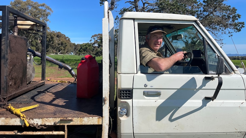 An older man is sitting in his ute on a farm
