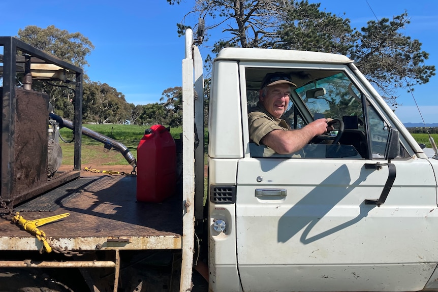 An older man is sitting in his ute on a farm