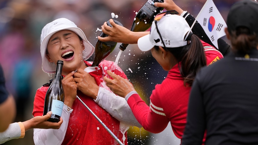 Amy Yang, in red shirt and white bucket hat, has champagne poured on her by other golfers after winning the PGA Championship.