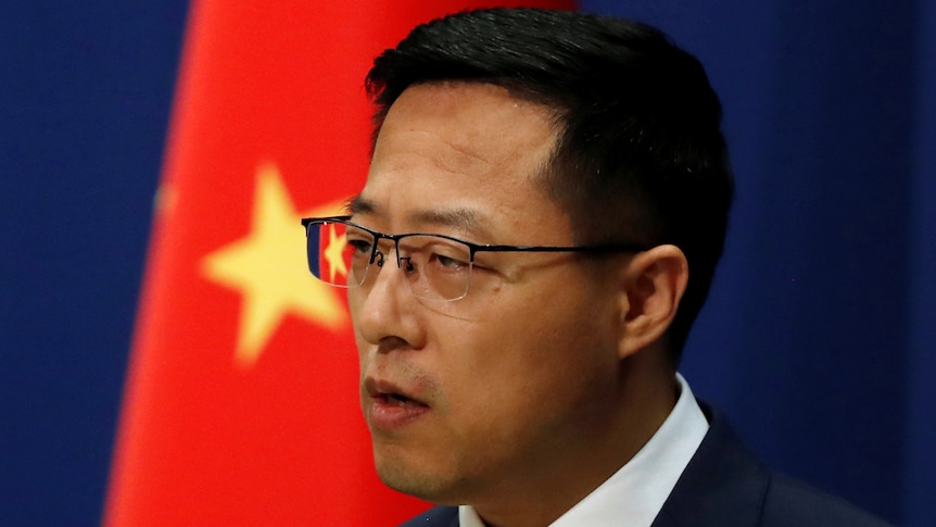 Man in a suit with a Chinese flag in the background.