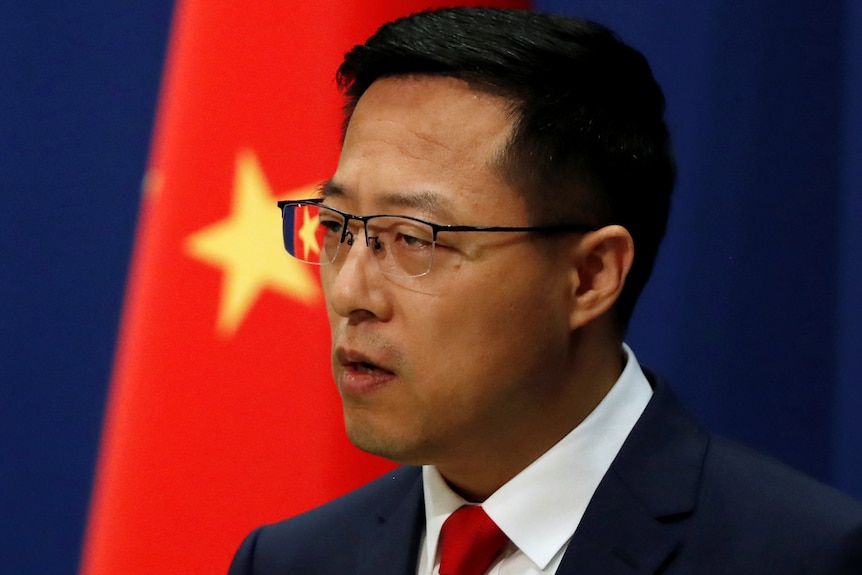 一名戴眼镜的男子站在中国国旗前。
