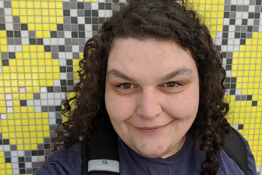 Claire Connors smiles while wearing a purple shirt in front of a yellow wall.