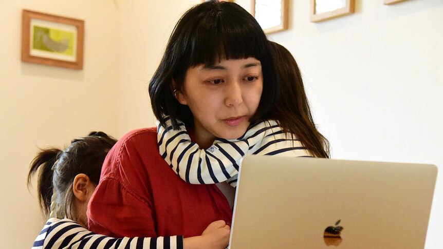 A woman at a computer with two small children hugging her