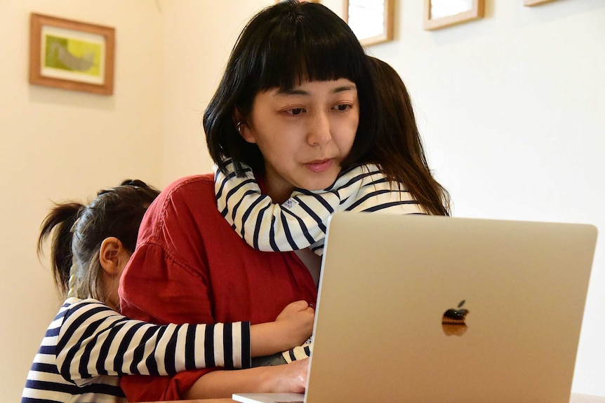 A woman at a computer with two small children hugging her