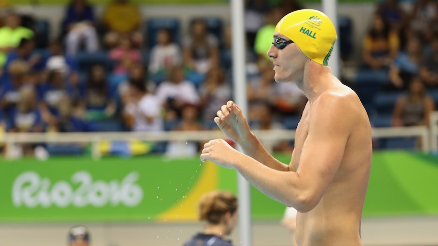An Australian Paralympic swimmer stands next to the pool with his goggles on and his surname 'Hall' on his swim cap.