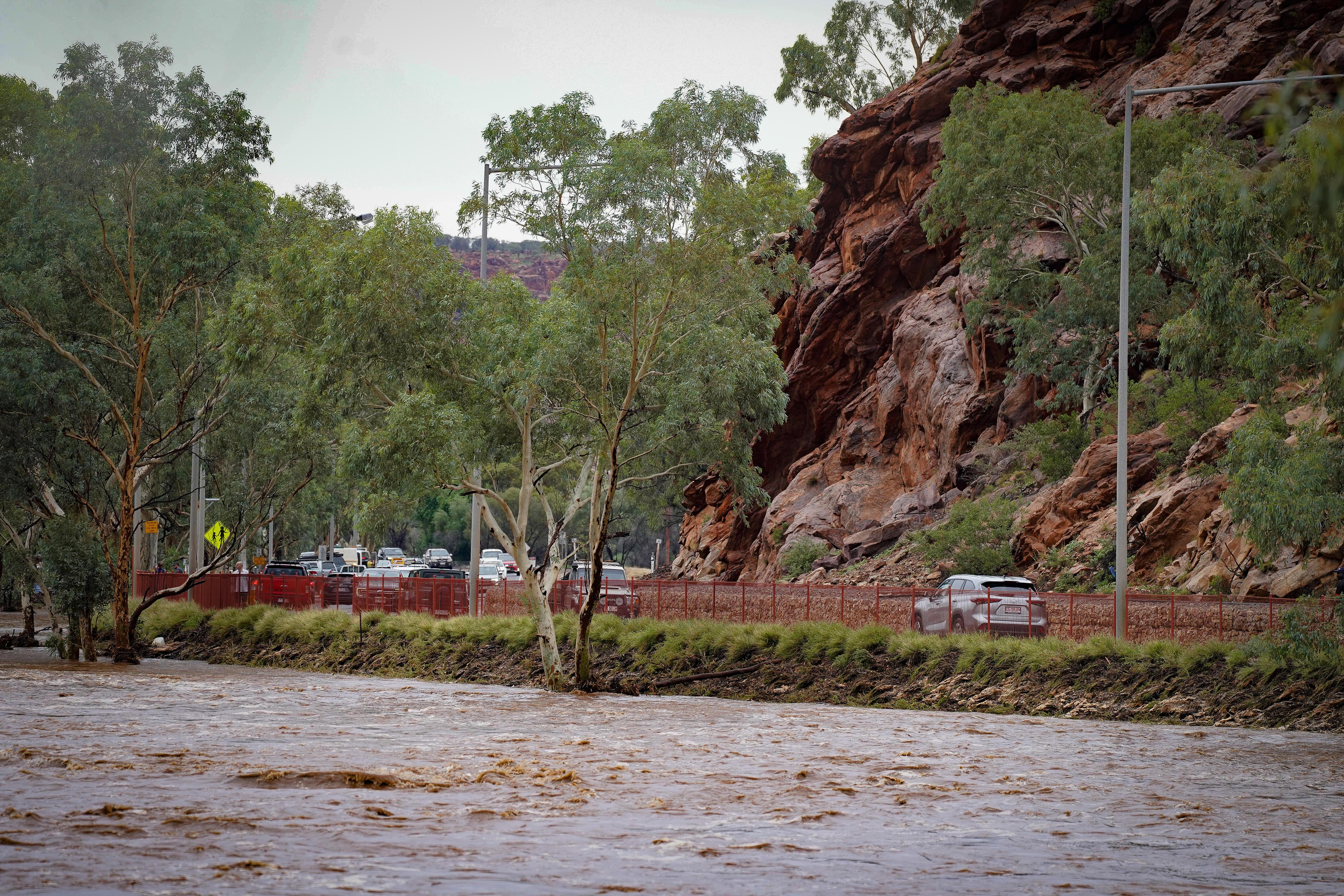 Um rio ao longo de margens verdes, uma estrada com muitos carros e um penhasco rochoso 