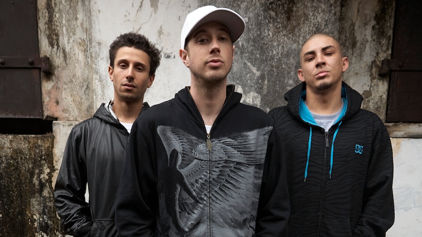 The three members of Bliss N Eso pose in a back alley
