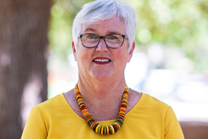 An older woman with short, white hair, wearing glasses and a bright coloured top.