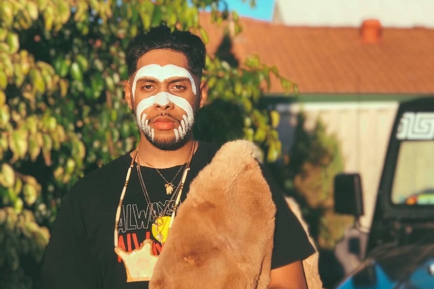 Derek Nannup with his face painted and a pelt over his shoulder.