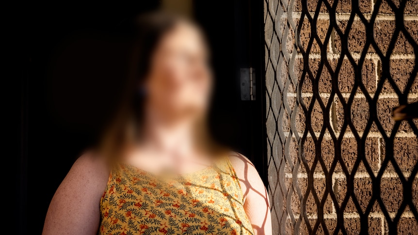 Woman with blurred face and hair looking out of a security screen door.
