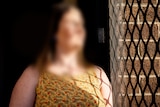 Woman with blurred face and hair looking out of a security screen door.
