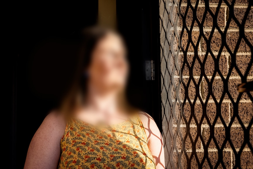 Woman with blurred face and hair looking out of a security screen door.