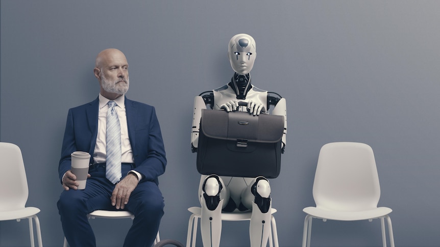 An older man in a suit sit next to a robot as they wait for a job interview