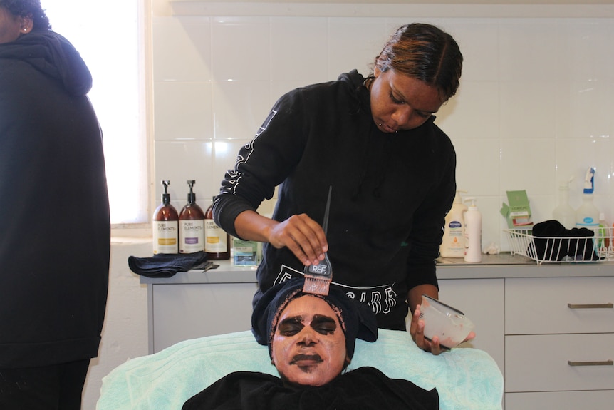 Student Lesharna Young applies a face mask to Anita Alice's face.