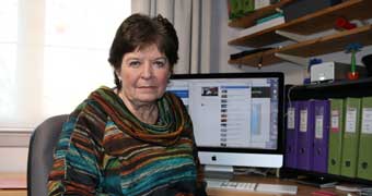 Charmian Gaud sits at a desk in front of her computer.