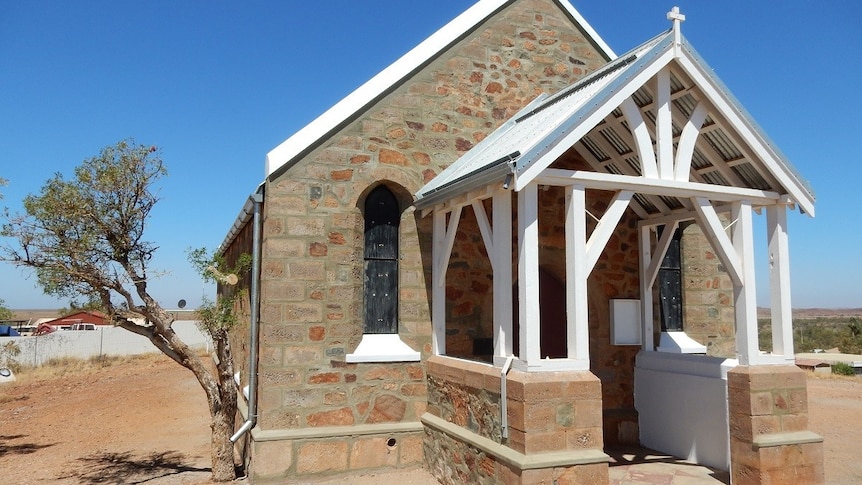 A small church stands surrounded by sand and clear blue skies.