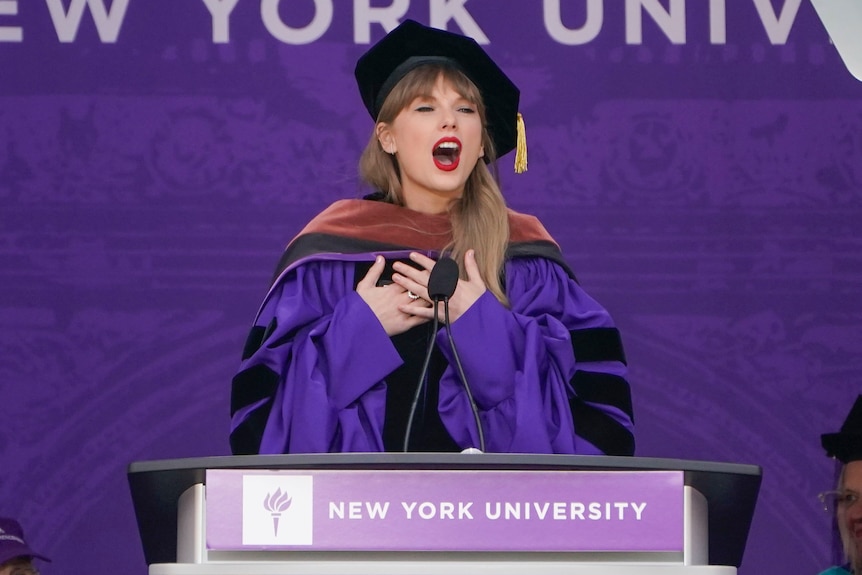 Taylor Swift speaks at lectern during a graduation ceremony.