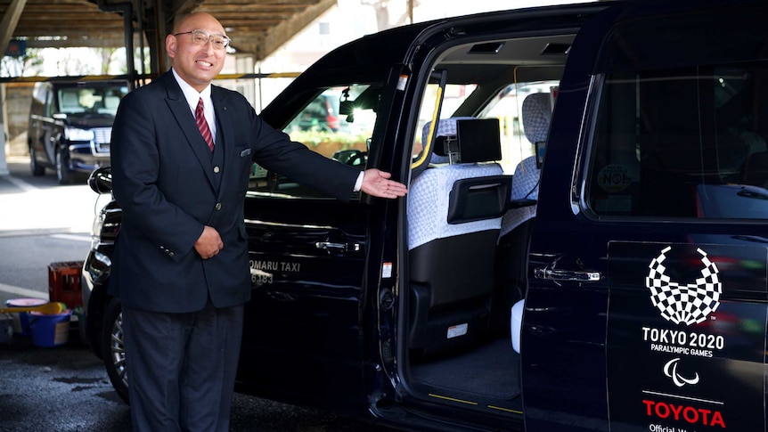 A Japanese taxi driver smiles next to his black cab