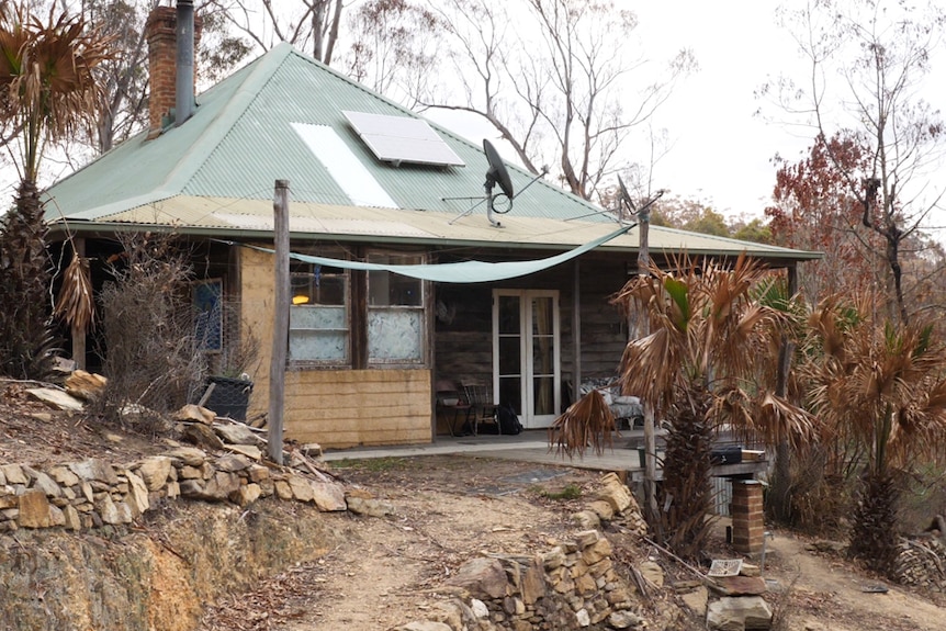 A small, old timber cottage set amongst burnt bush