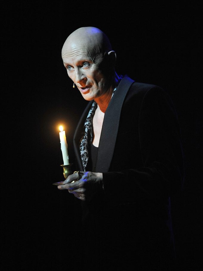 Richard O'Brien holding a candle on a dark stage