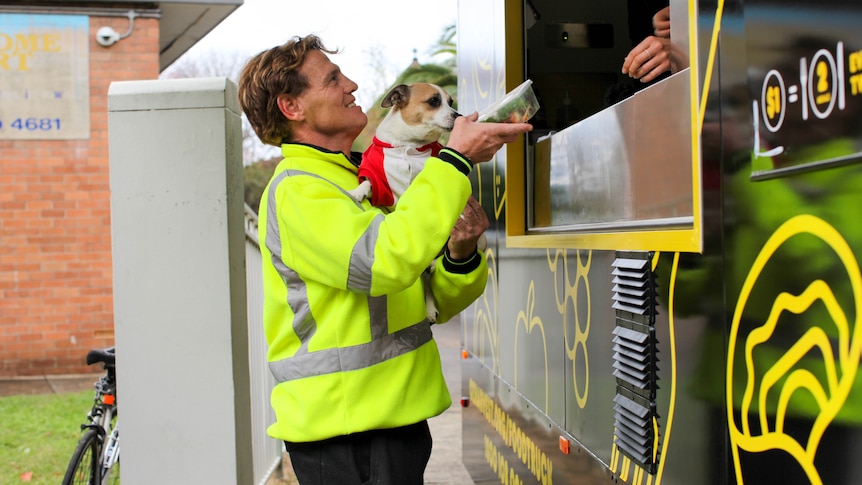 Man is handed some food as he holds his dog in front of the Ozharvest food truck