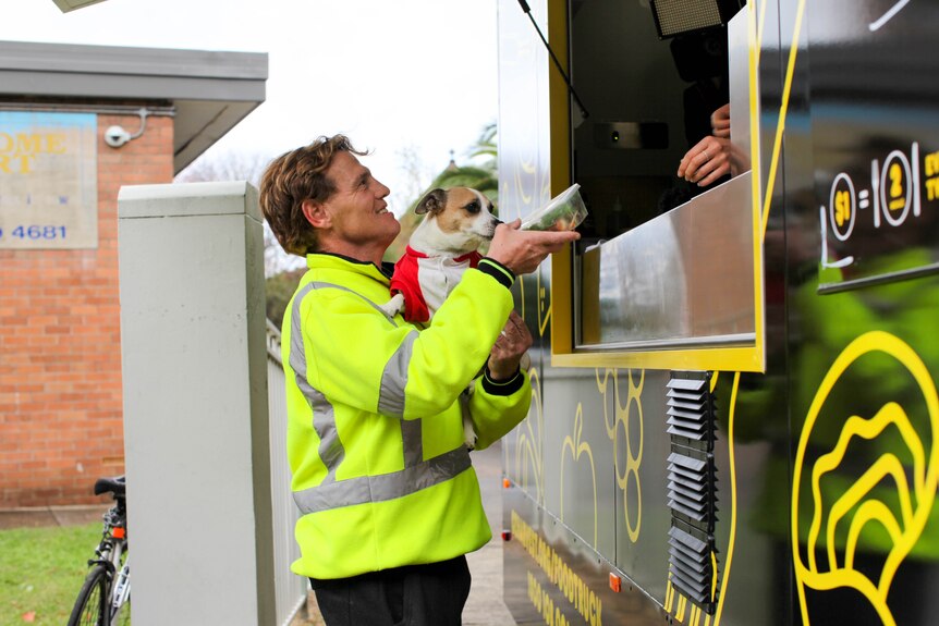 Man is handed some food as he holds his dog in front of the Ozharvest food truck