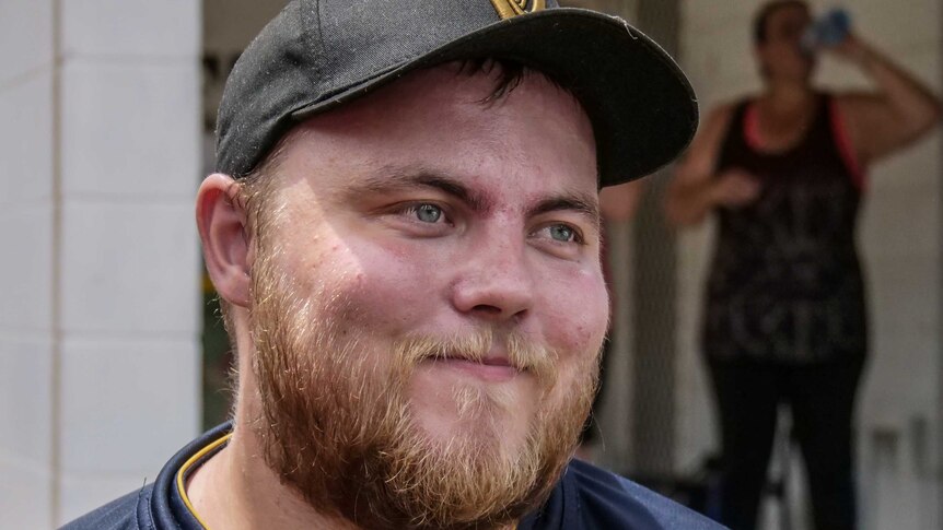 A man with a baseball cap and facial hair stares off to the side.